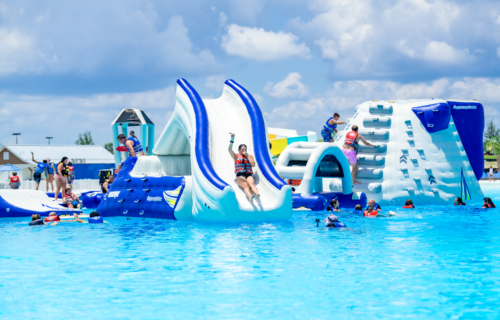 A girl sliding down an inflatable slide attached to a water obstacle course in the blue waters of the lagoon.